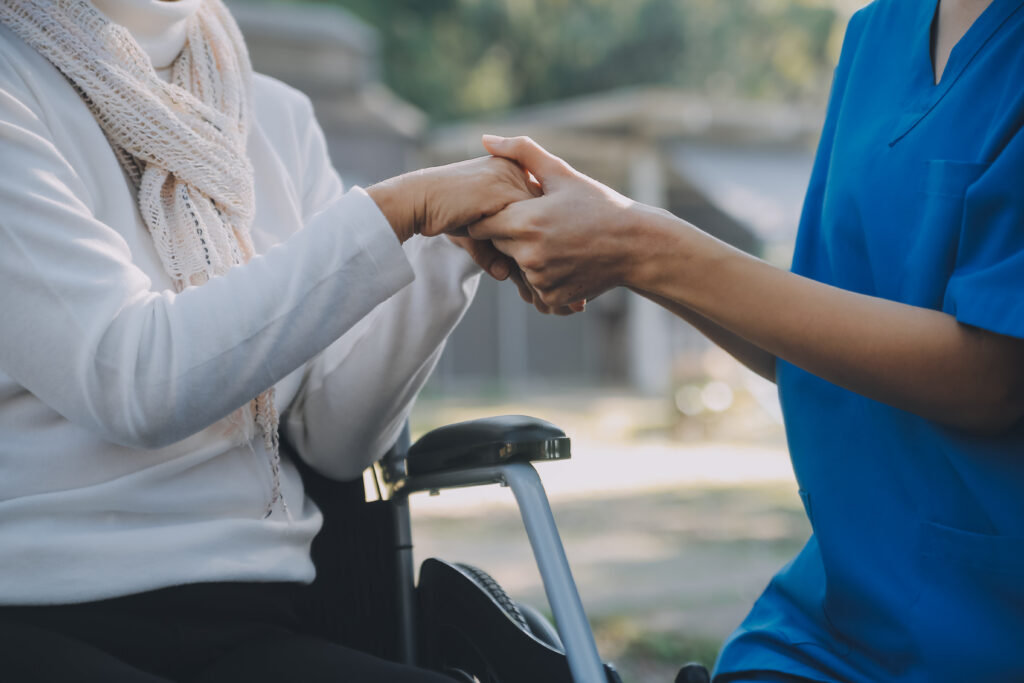 A carer offering a reassuring hand to a wheelchair user.